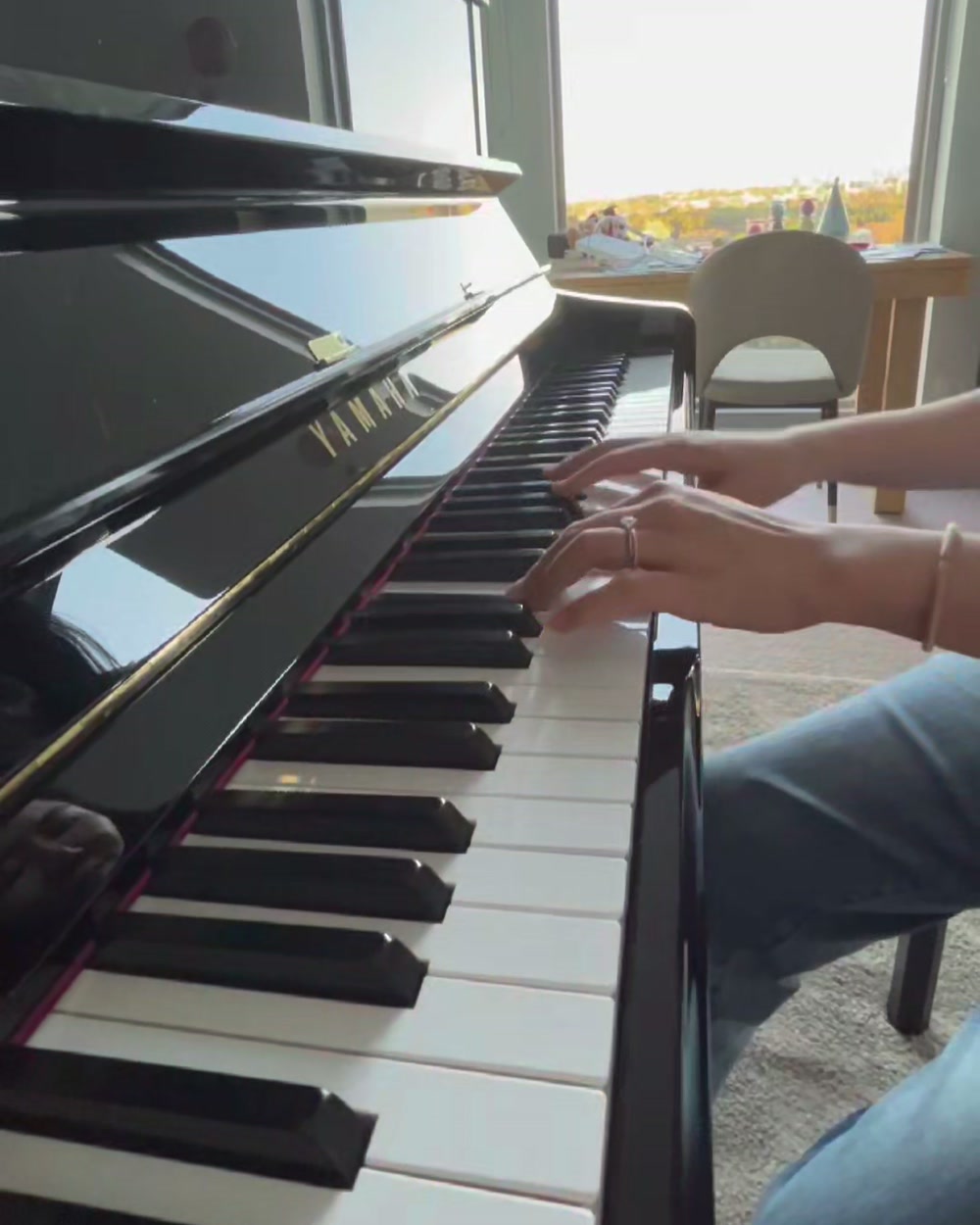 Hands playing the upright, seen from the side, the park in the window behind